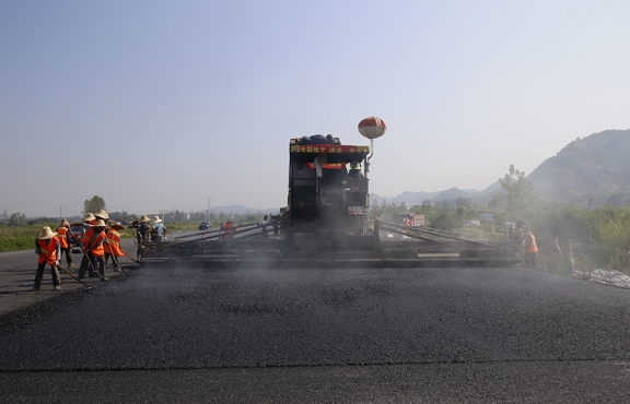 2019年8月，宜春經(jīng)開區(qū)S311路面攤鋪現(xiàn)場(chǎng)，工友們輔助路面兩側(cè)的分料、補(bǔ)窩等作業(yè)